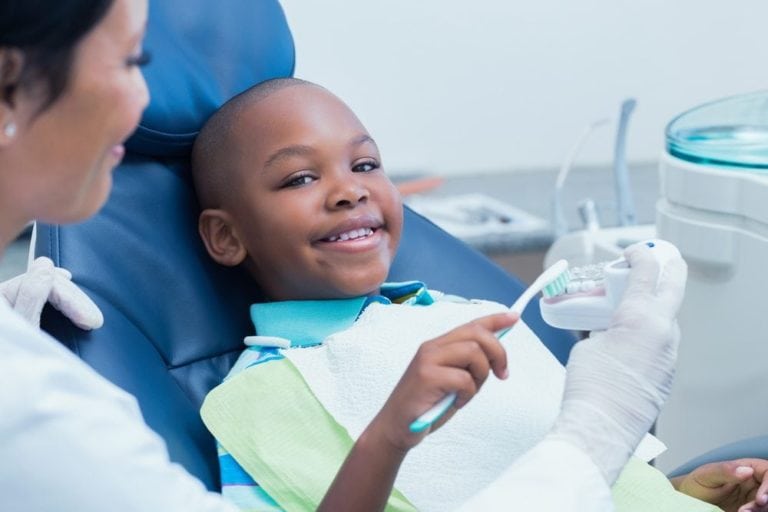 young boy smiling while brushing fake teeth at the dentist