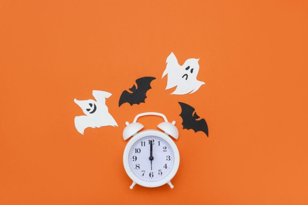 white clock on an orange background surrounded by ghosts and bats