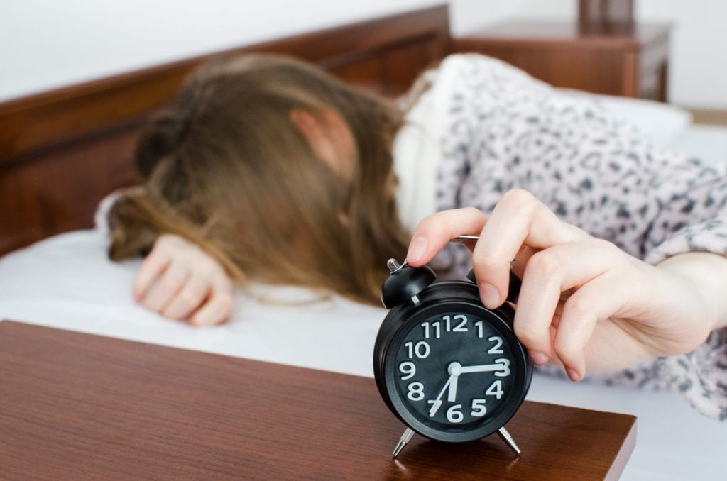 teenage girl hitting snooze on her alarm clock