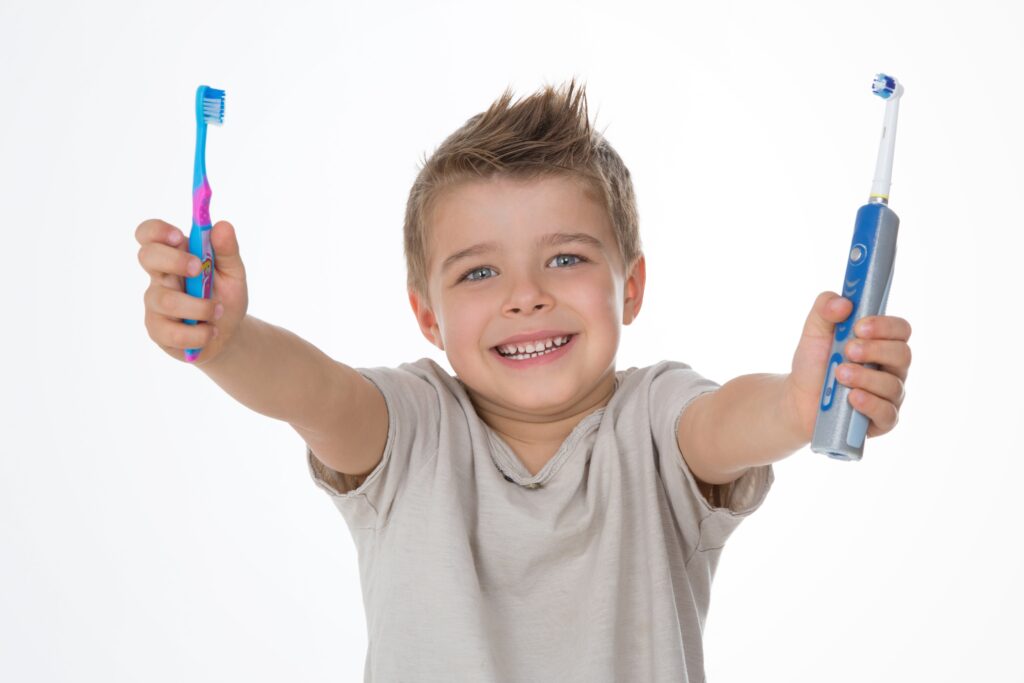 young boy holding an electric toothbrush in one hand and a manual toothbrush in the other