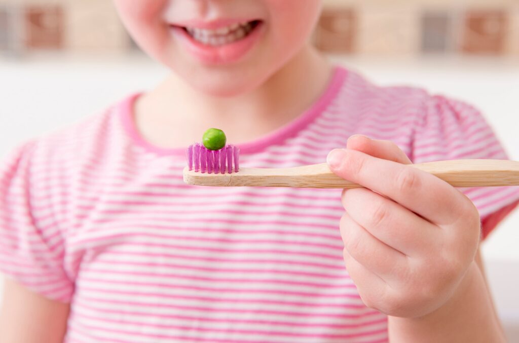 young girl with a pea on her toothbrush indicating proper toothpaste use
