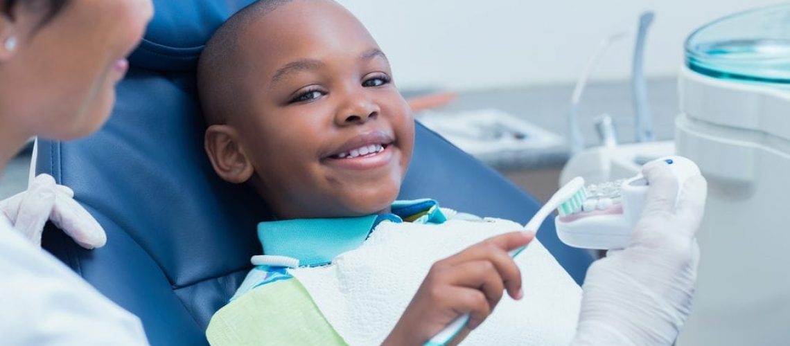young boy smiling while brushing fake teeth at the dentist
